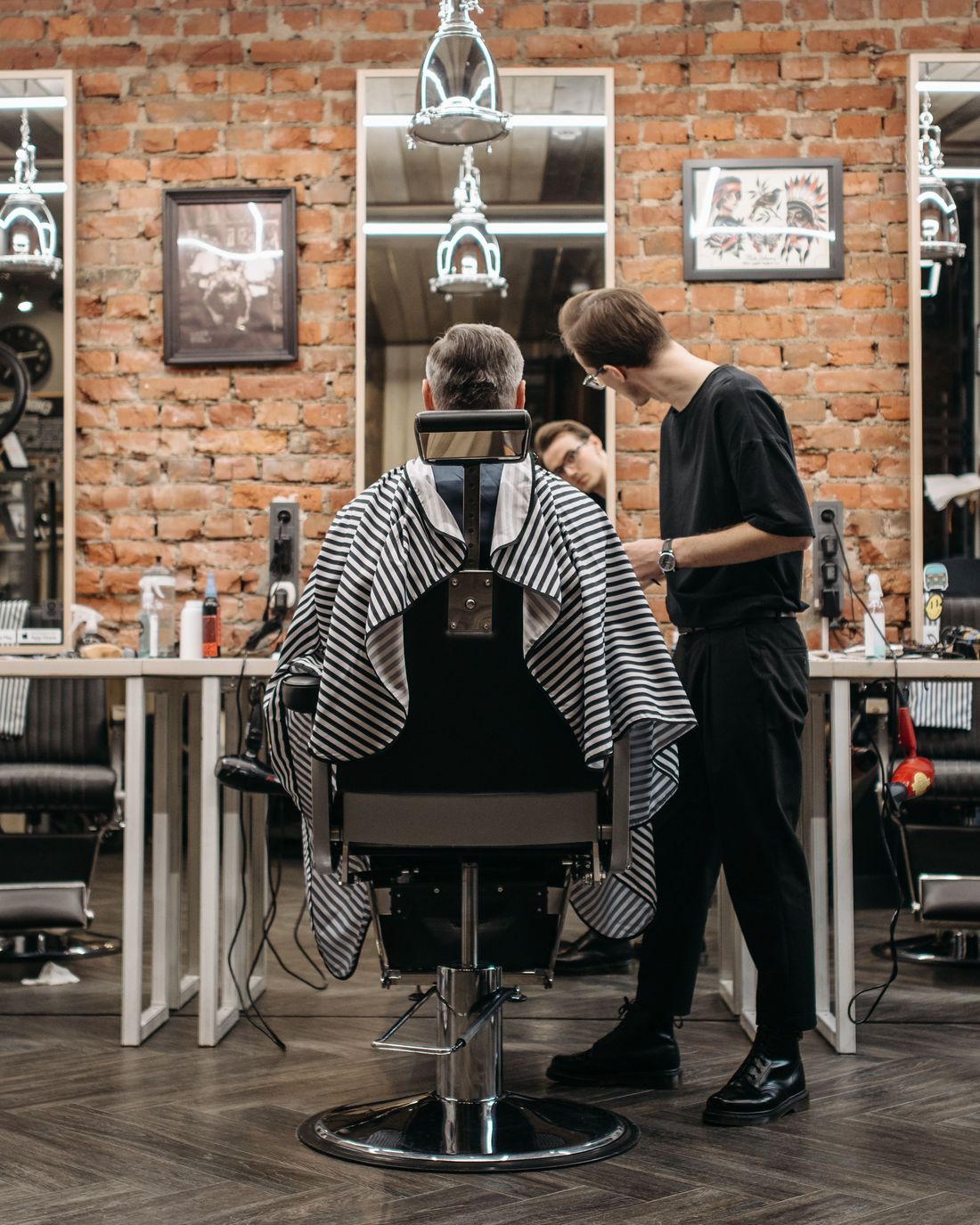A barber cutting a client's hair in a brick barbershop
