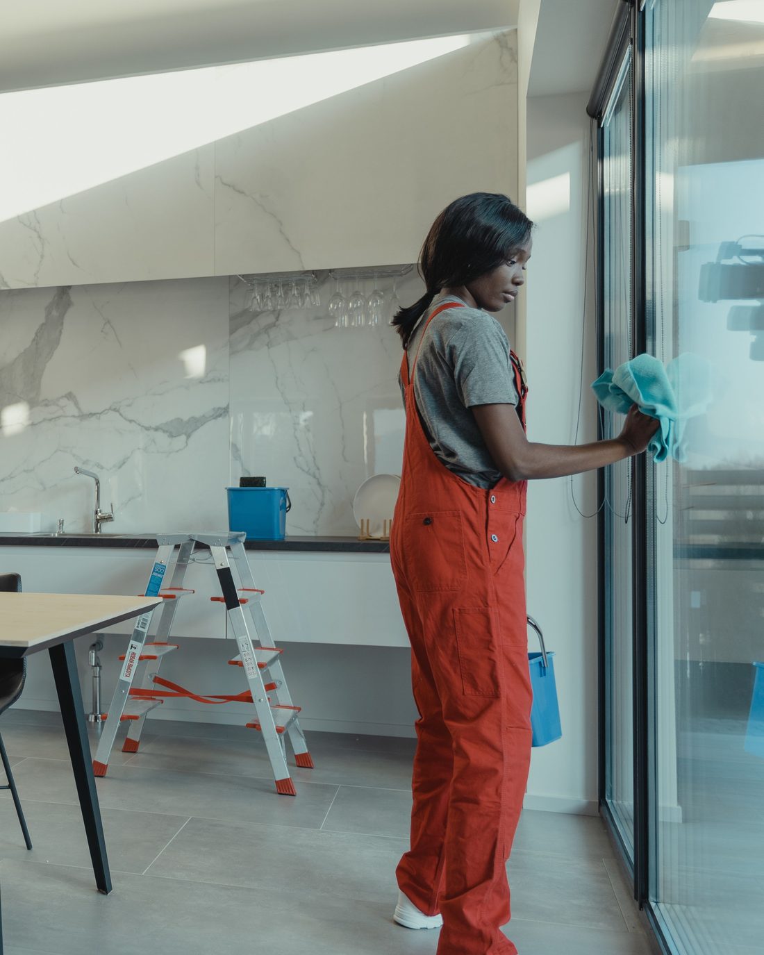 A professional cleaner in overalls wiping down a glass door in a bright, modern kitchen